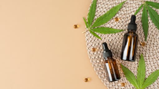 Cannabis leaves and amber dropper bottles on a woven surface