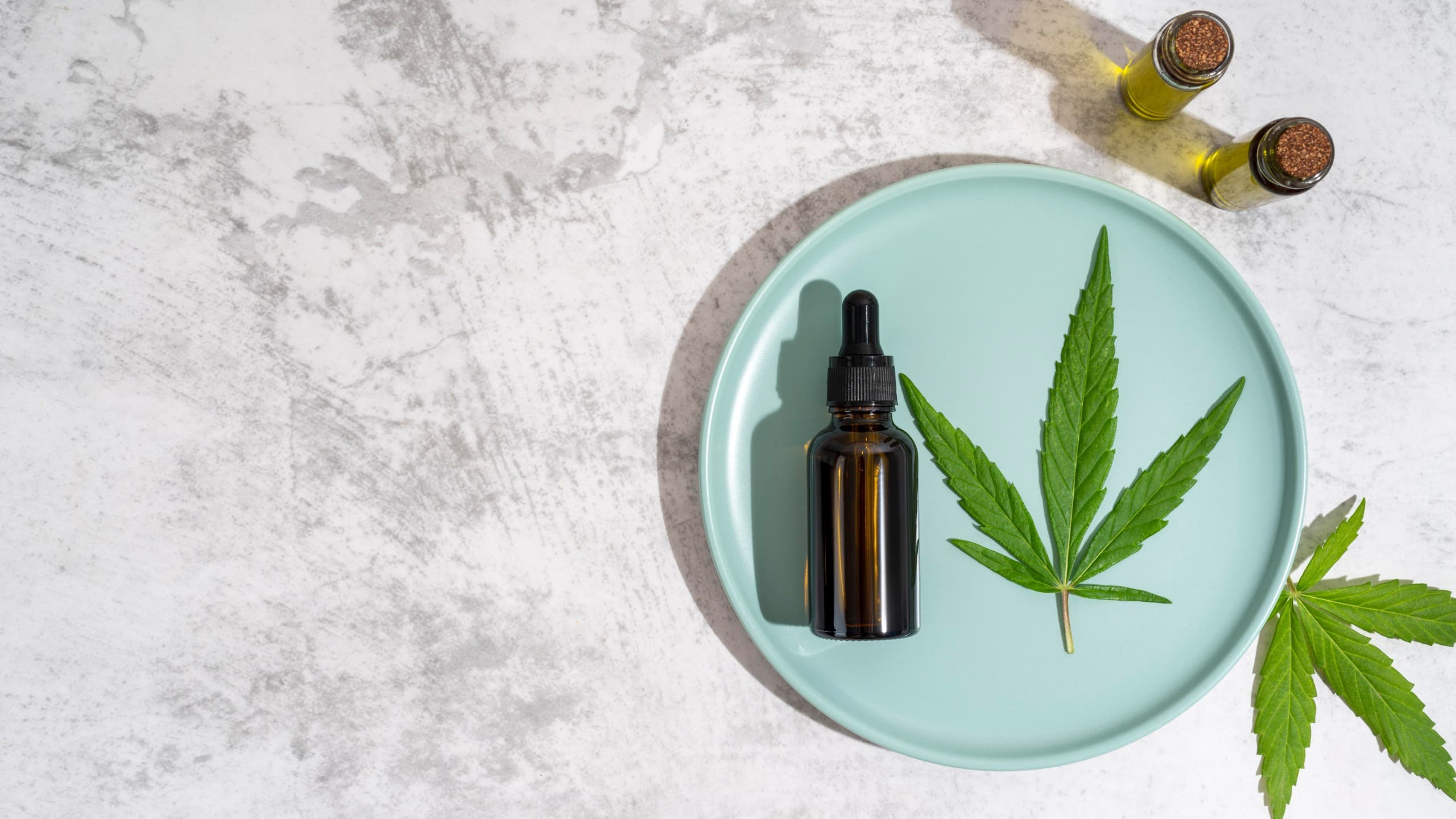 CBD dropper bottle and cannabis leaf on a marble surface